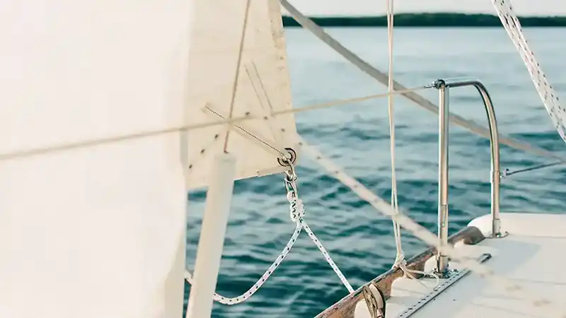 white sail and edge of a boat with a railing. choppy water surface.